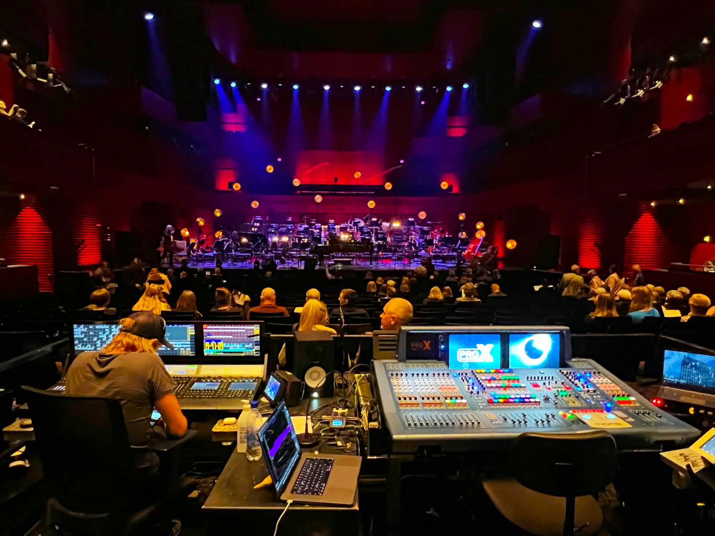 Technician operates soundboard in concert hall control booth.