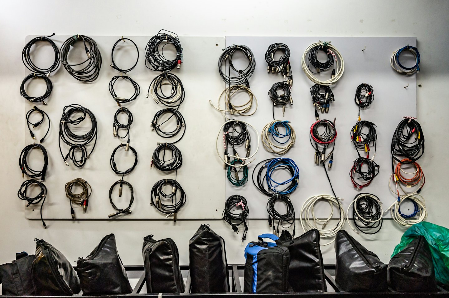 Coiled audio and video cables organized on a wall panel with bags below.